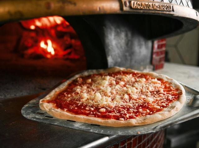 A pizza topped with cheese and tomato sauce being transferred on a peel into a wood-fired oven.