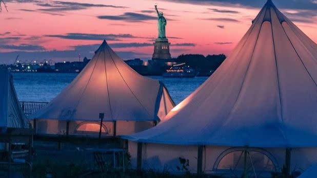 Glamping tents on Governors Island with a view of the Statue of Liberty at sunset