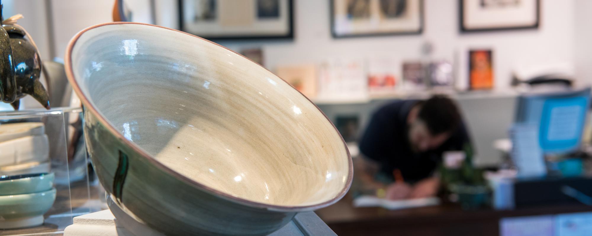 A cream and sage ceramic bowl on display in the Woodstock Byrdcliffe Guild Shop
