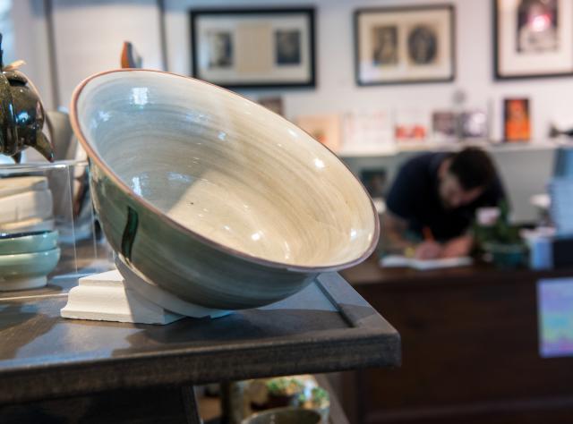 A cream and sage ceramic bowl on display in the Woodstock Byrdcliffe Guild Shop