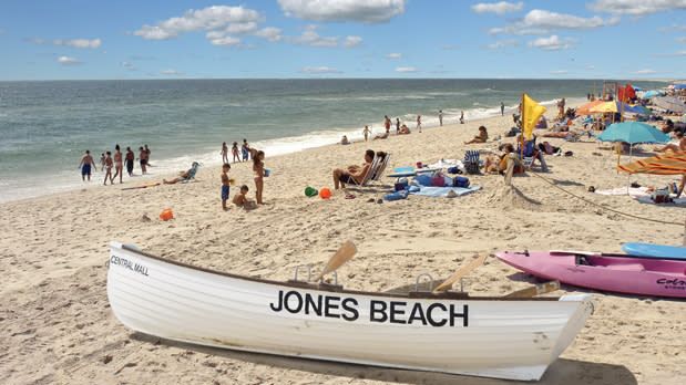 Canoe resting on the beach shore, view of people sunbathing and walking toward ocean