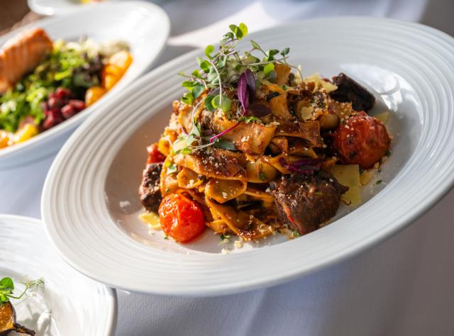 A plate of pasta topped with leafy greens at Sagamore Resort
