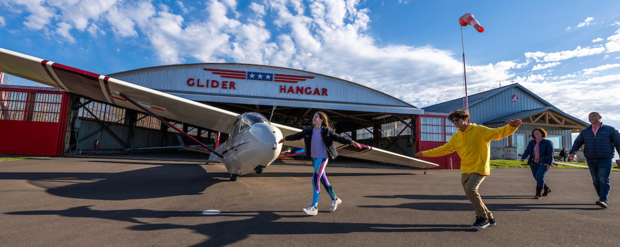 A group of people walking towards a parked glider in a hangar at the National Soaring Museum in Elmira, New York.