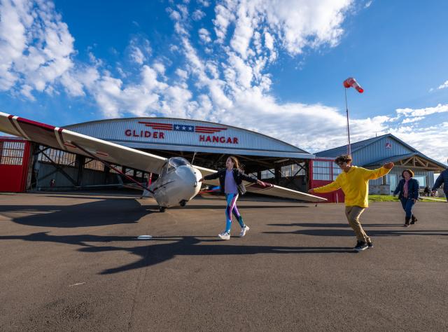 A group of people walking towards a parked glider in a hangar at the National Soaring Museum in Elmira, New York.